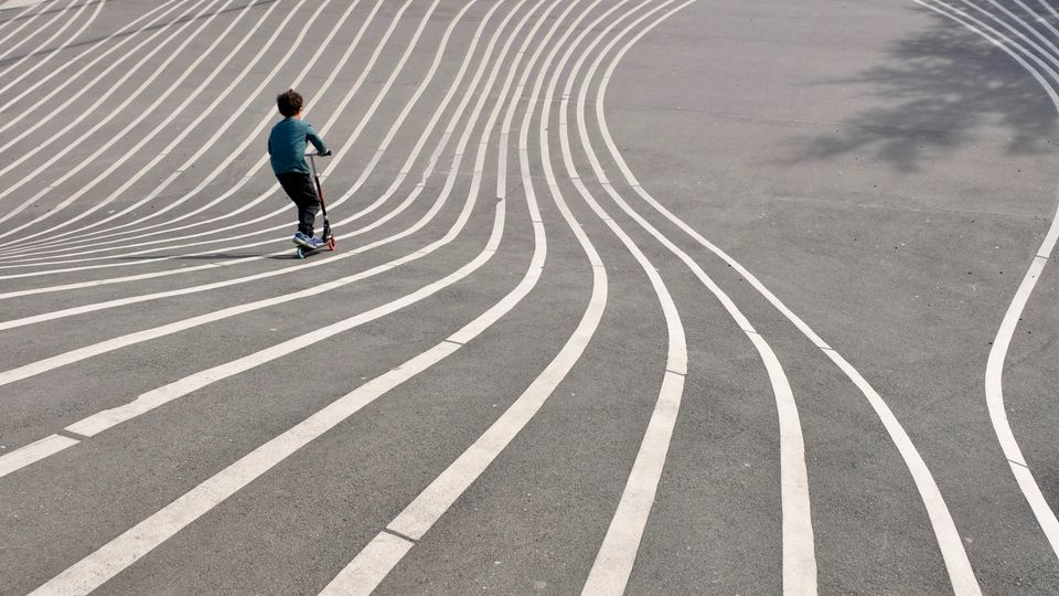 Boy on a scooter, travelling along curvy lines on sloping asphalt.