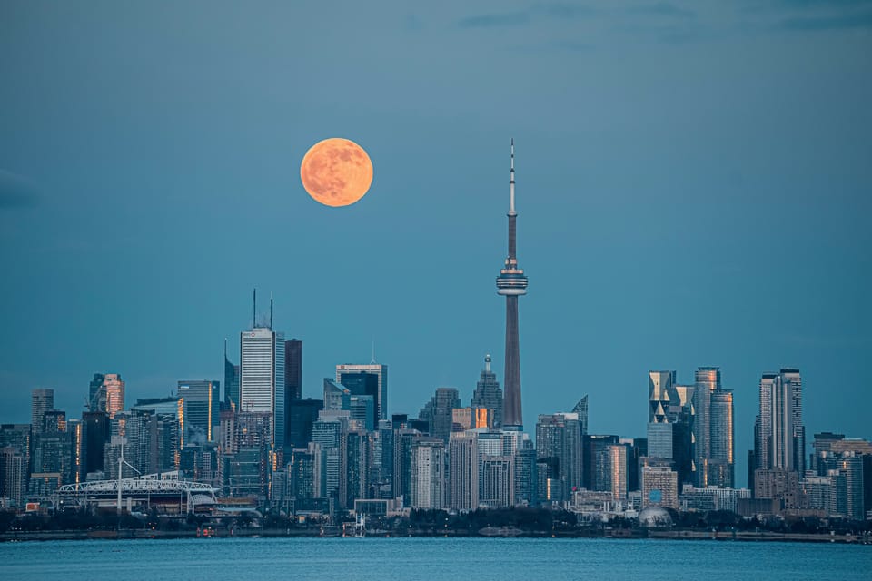 Toronto skyline at twilight, the moon suspended above the city.